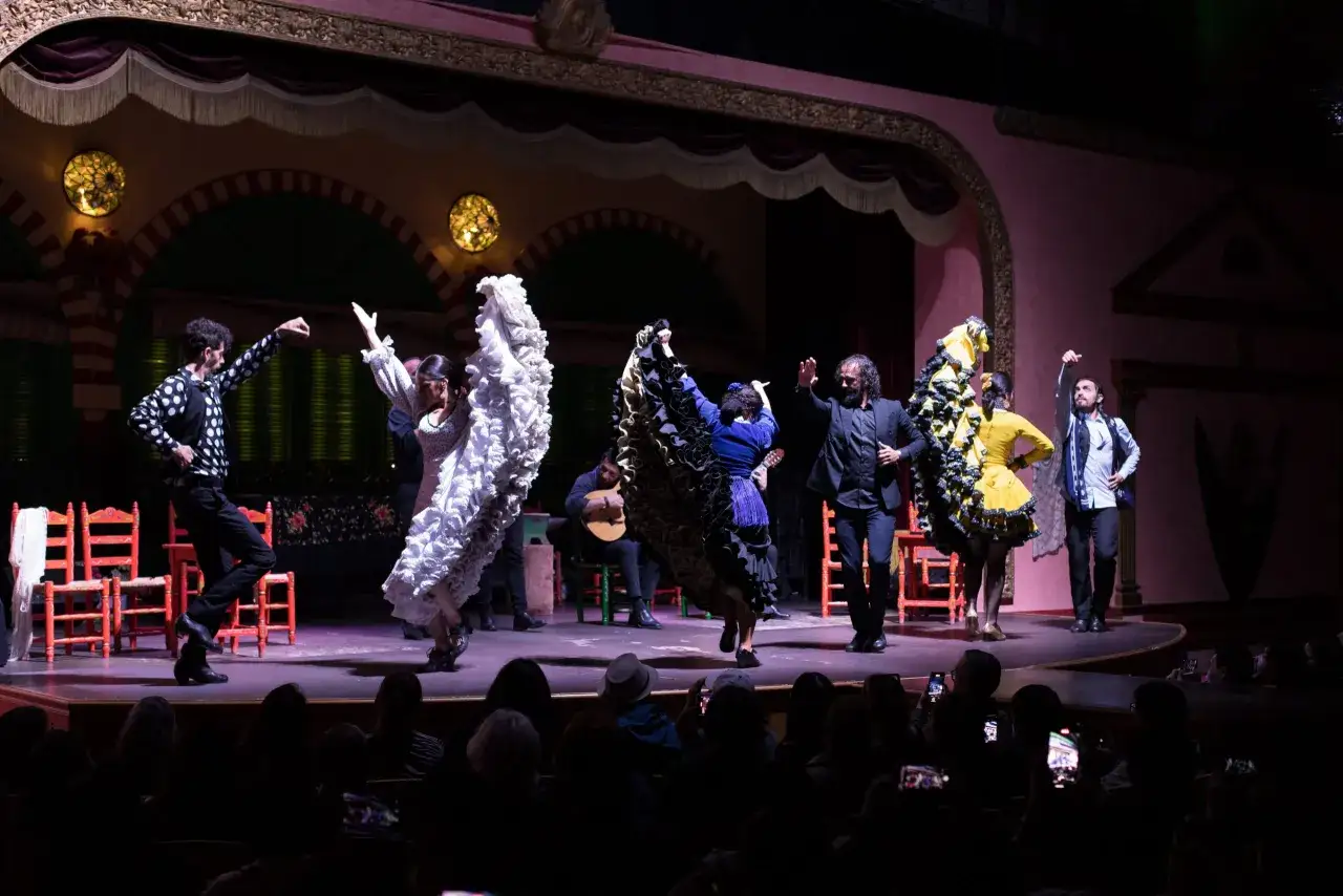 Artistas ejecutan un vibrante danse flamenco en un escenario, con faldas voluminosas y trajes llamativos.