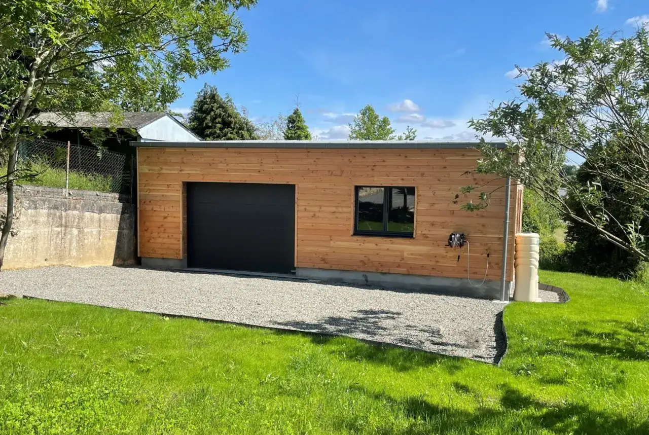 Nouveau garage en bois avec porte noire et fen&ecirc;tre. Un agrandissement qui s'int&egrave;gre parfaitement au paysage verdoyant.