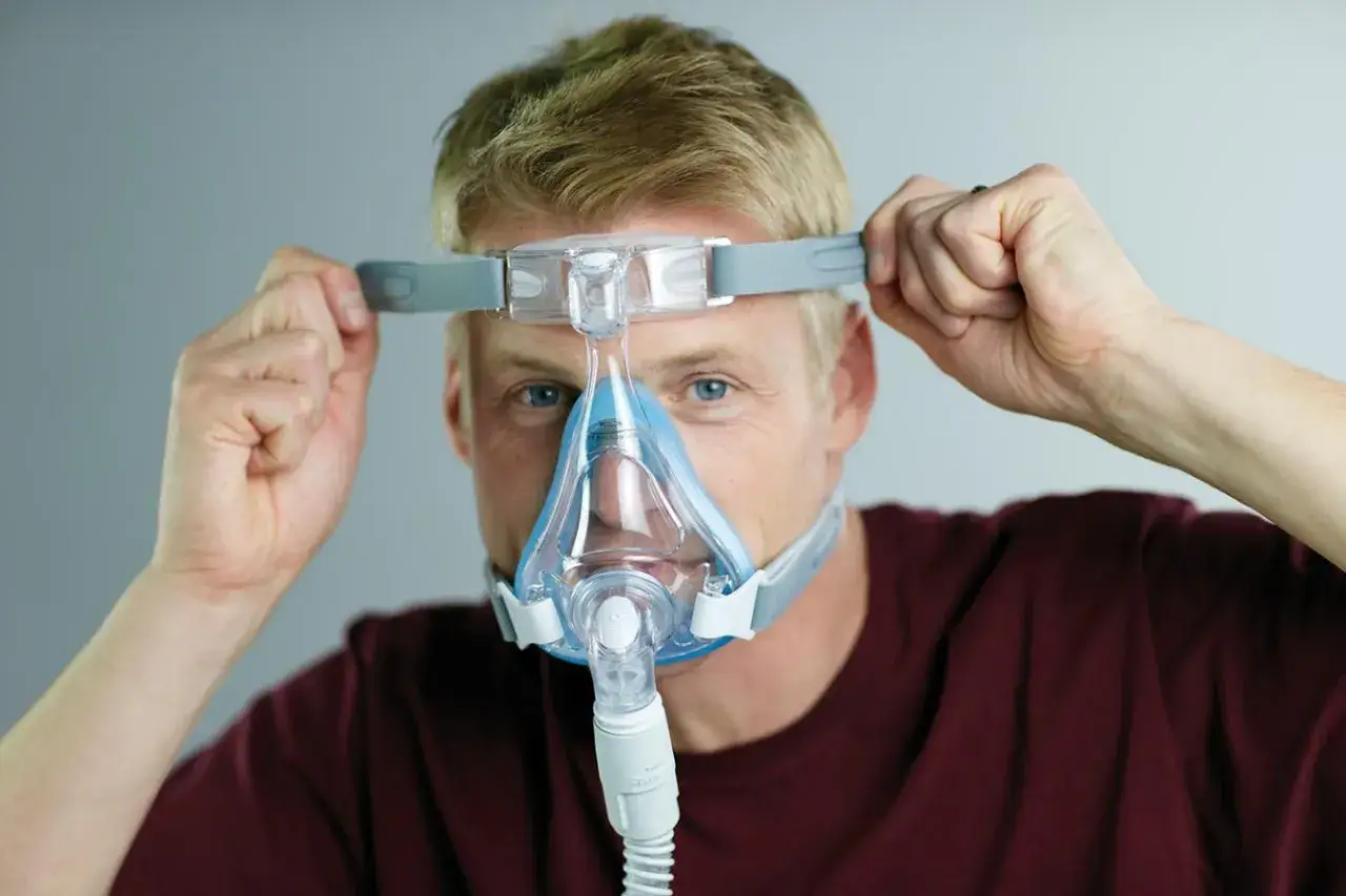 Mężczyzna zakłada maskę CPAP, kt&oacute;ra pomaga na bezdech senny. To skuteczne rozwiązanie dla spokojnego snu.
