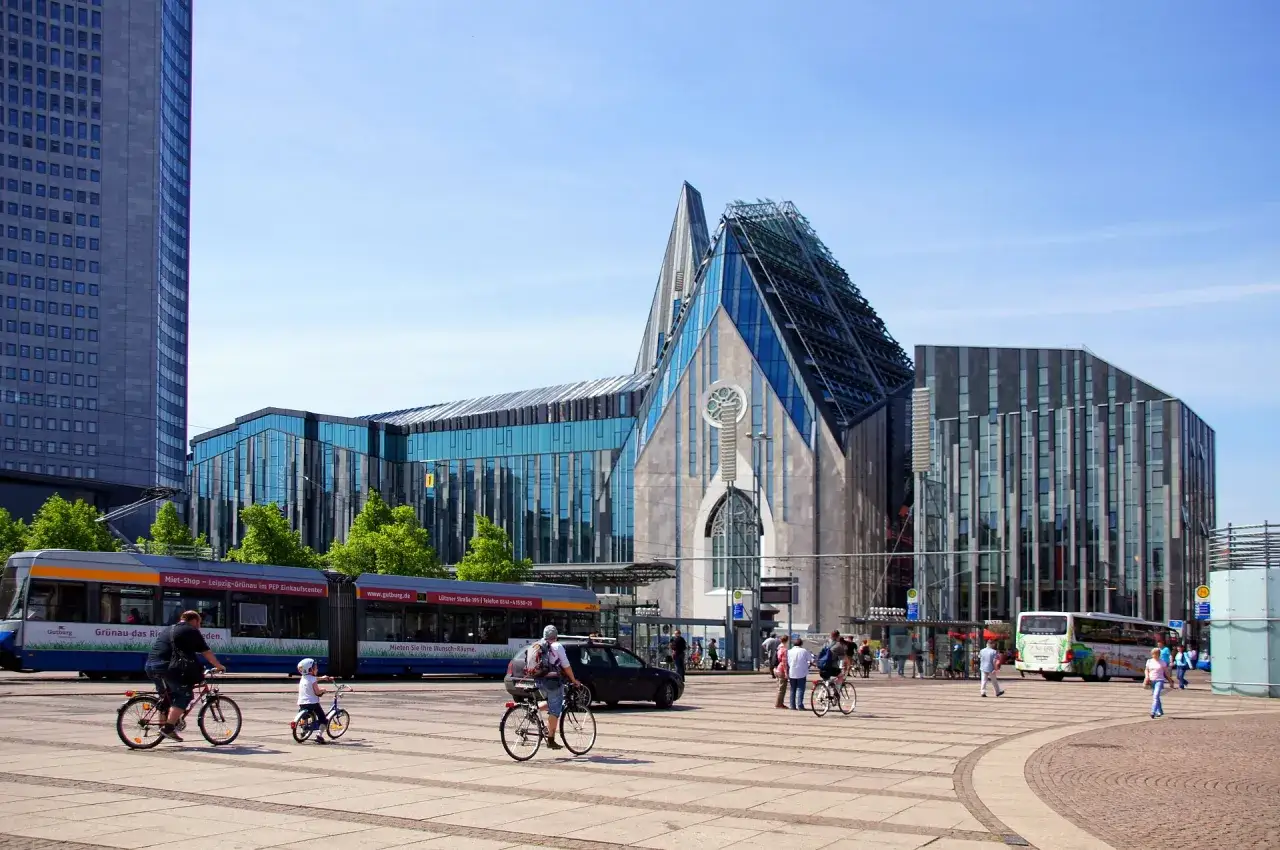 Moderne Architektur in Leipzig: Ein Mann mit Kind auf Fahrrädern, eine Straßenbahn und ein Bus auf einem Platz. Tolle Leipzig Tipps für deinen Besuch!