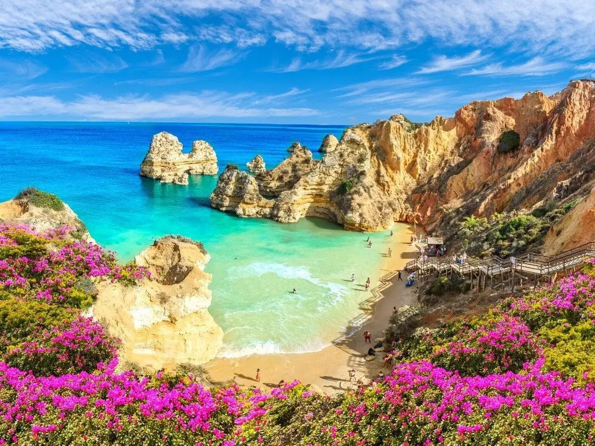 Ein traumhafter Lagos Strand mit t&uuml;rkisfarbenem Wasser, Felsformationen und bl&uuml;henden Bougainvillea. Menschen genie&szlig;en das Meer.