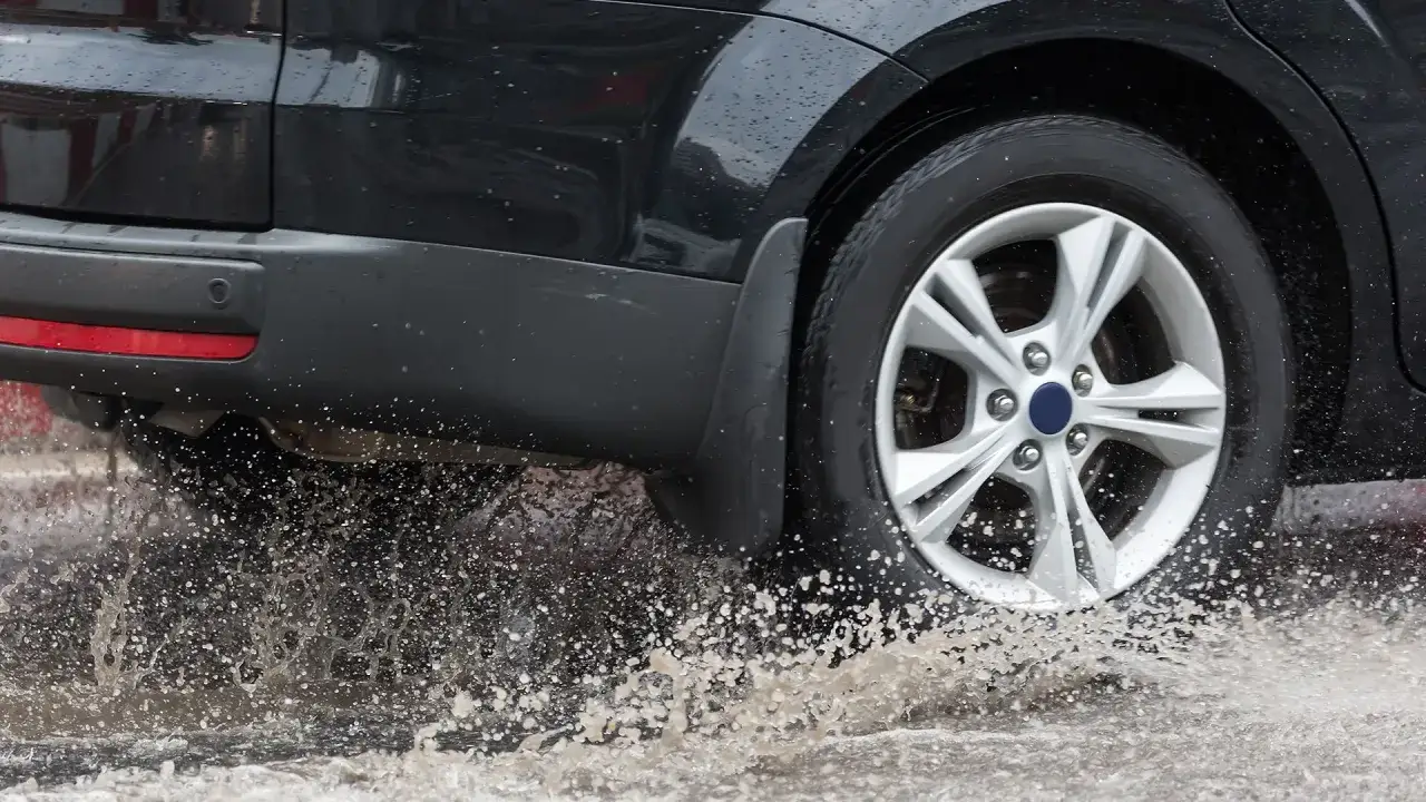 Une voiture noire roule dans une flaque d'eau, projetant des éclaboussures. Peut-on changer un seul pneu dans cette situation ?