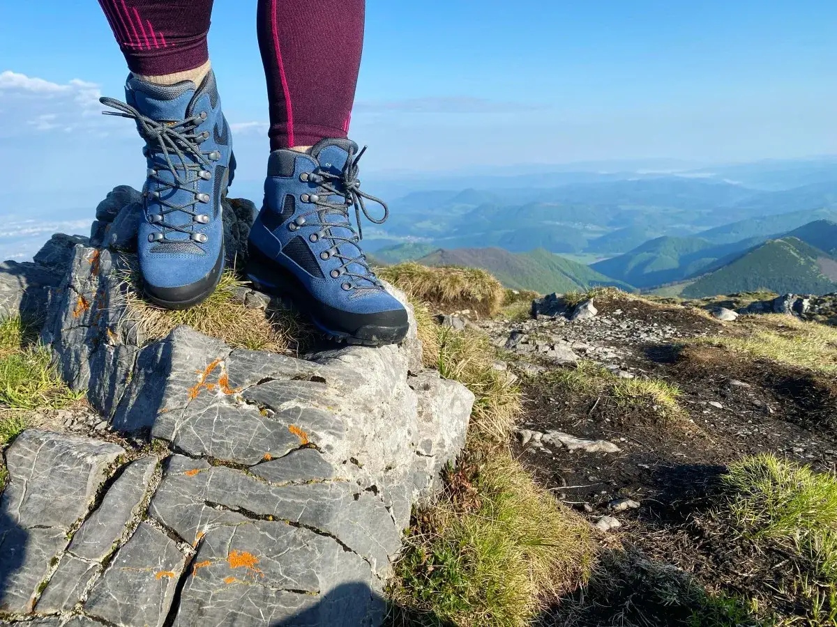 Niebieskie, wysokie aku buty na szczycie g&oacute;ry, gotowe na wędr&oacute;wkę po malowniczych, zielonych wzg&oacute;rzach.