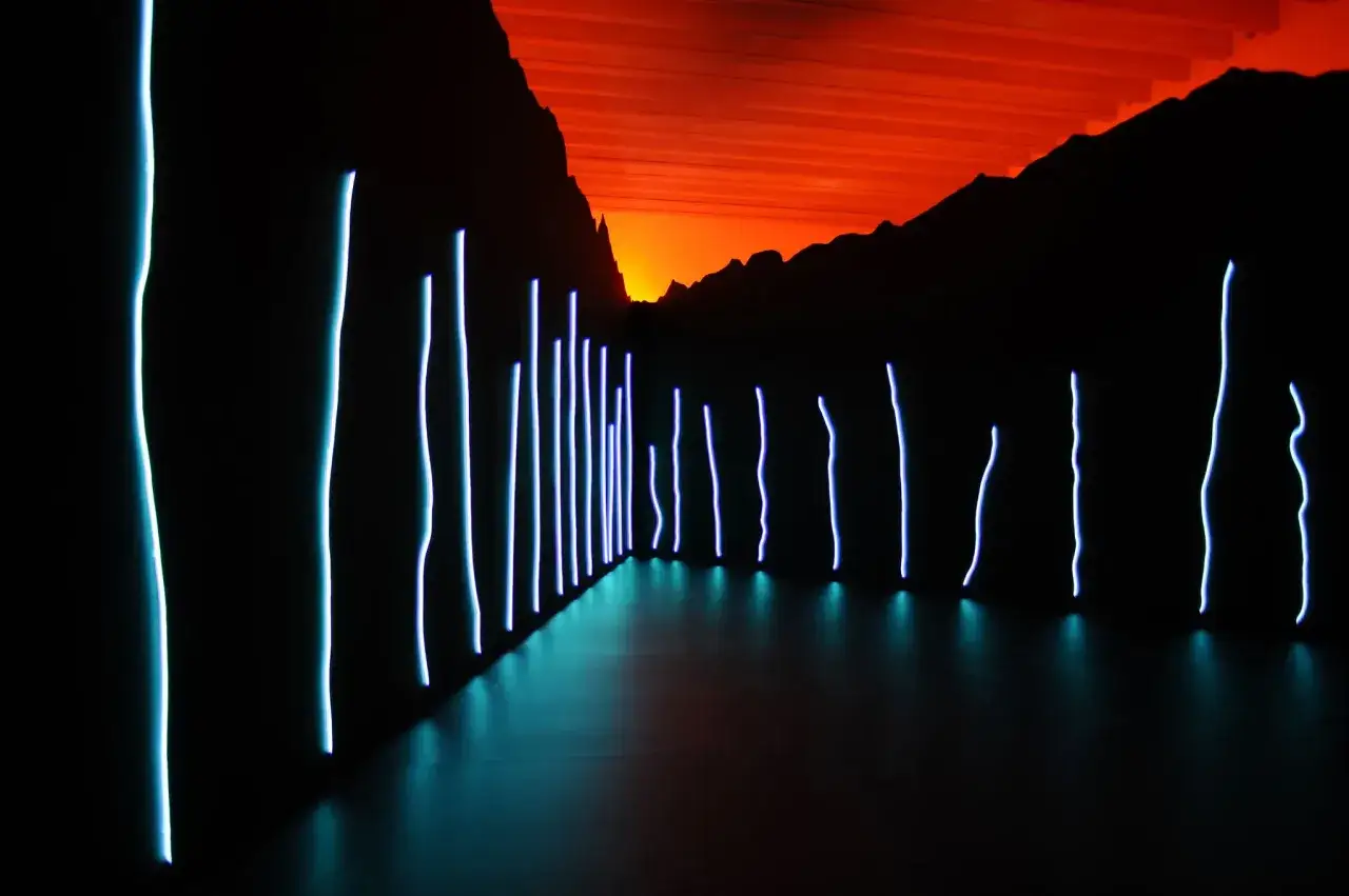 Installation lumineuse de Claude L&eacute;v&ecirc;que : des n&eacute;ons bleus cr&eacute;ent un chemin vers un ciel orang&eacute;, &eacute;voquant un paysage onirique.