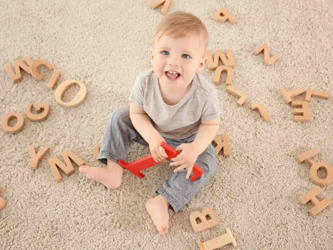 Bambino sorridente circondato da lettere di legno, forse un segno che la lallazione quando inizia.