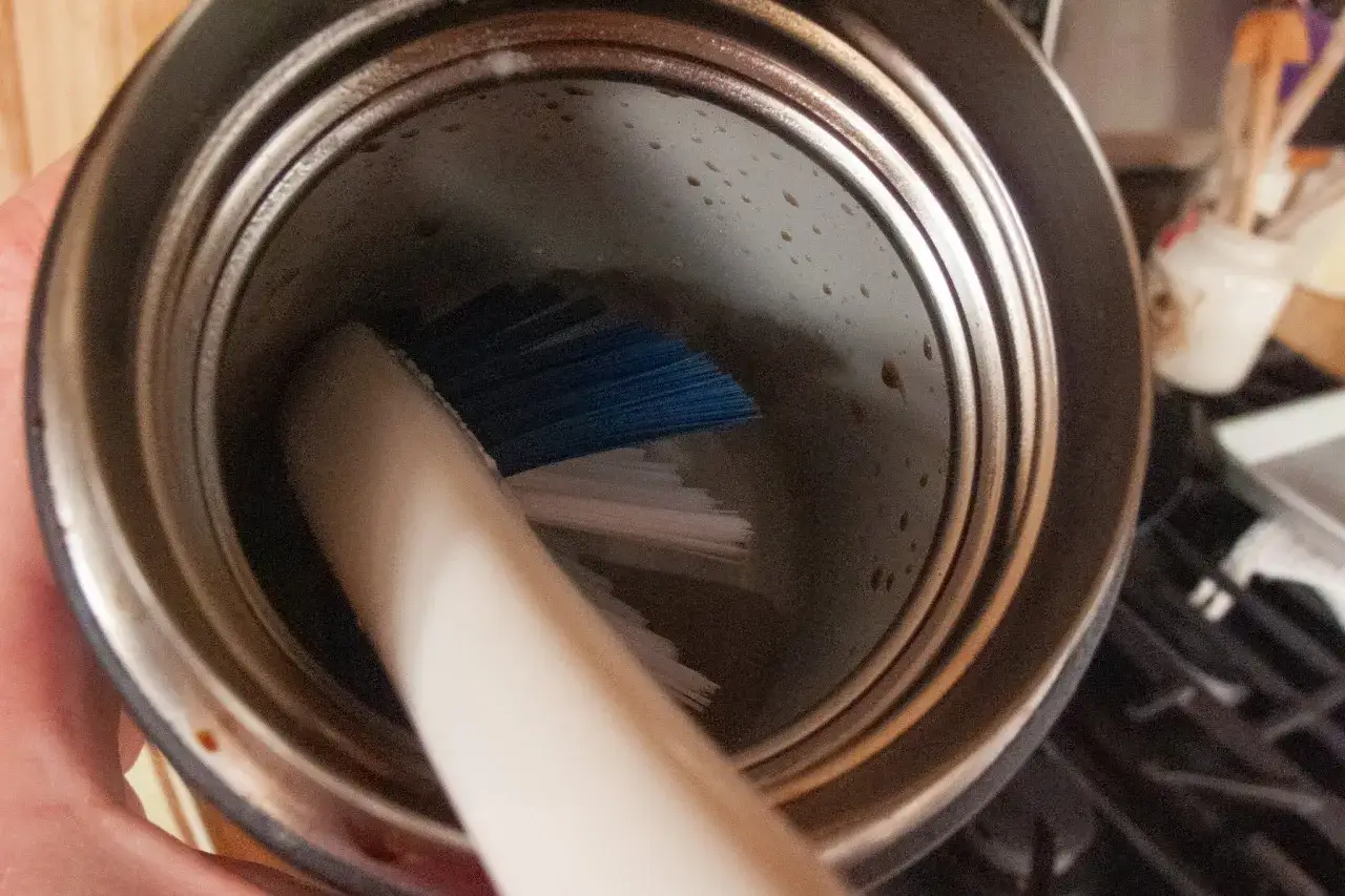 Brosse bleue &agrave; l'int&eacute;rieur d'une gourde inox pour un nettoyage en profondeur.