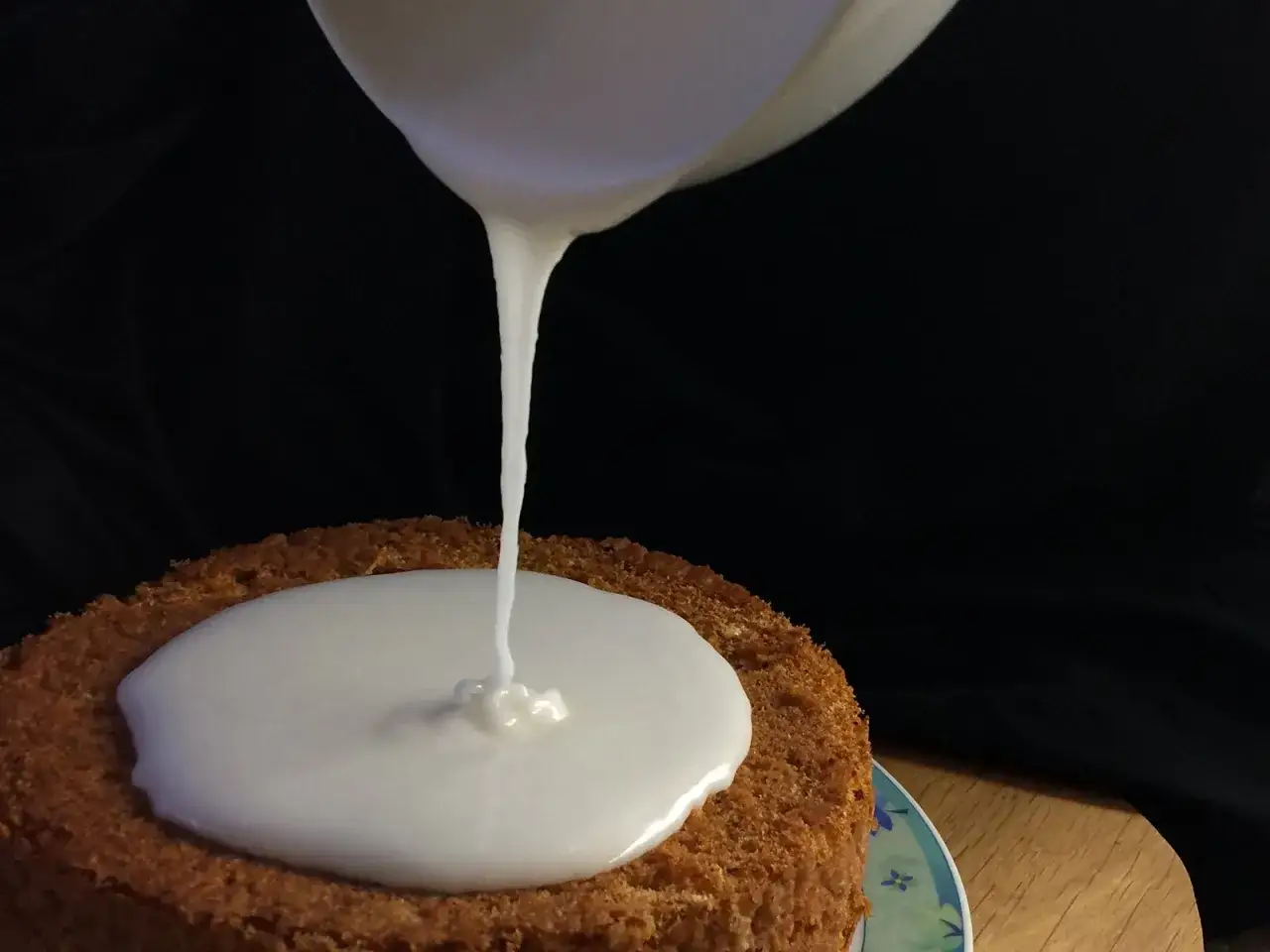 Ein Kuchen wird mit zuckerguss mit milch überzogen. Der weiße Guss fließt langsam über den braunen Kuchen.