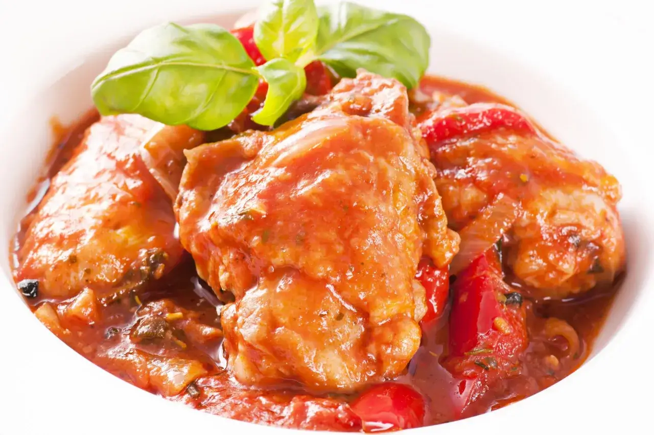 Sabroso pollo con tomate, cocinado a fuego lento con hierbas y servido en un cuenco blanco.