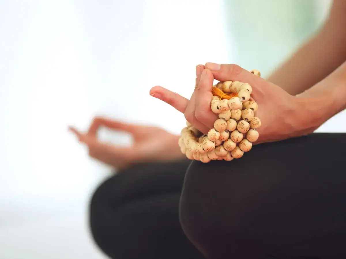 Manos meditando con un mala de madera, símbolo de paz interior y conexión espiritual.
