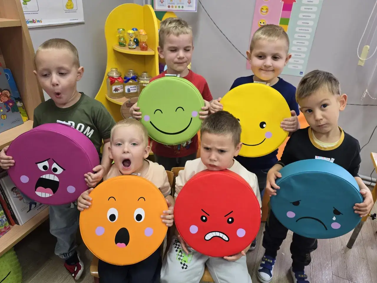 Dzieci w przedszkolu pokazują emocje na okrągłych poduszkach: radość, złość, smutek, zaskoczenie.