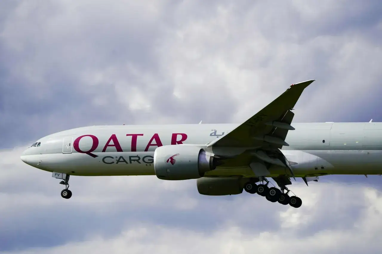 Samolot Qatar Airways Cargo z wysuniętym podwoziem, gotowy do lądowania. W tle chmury.