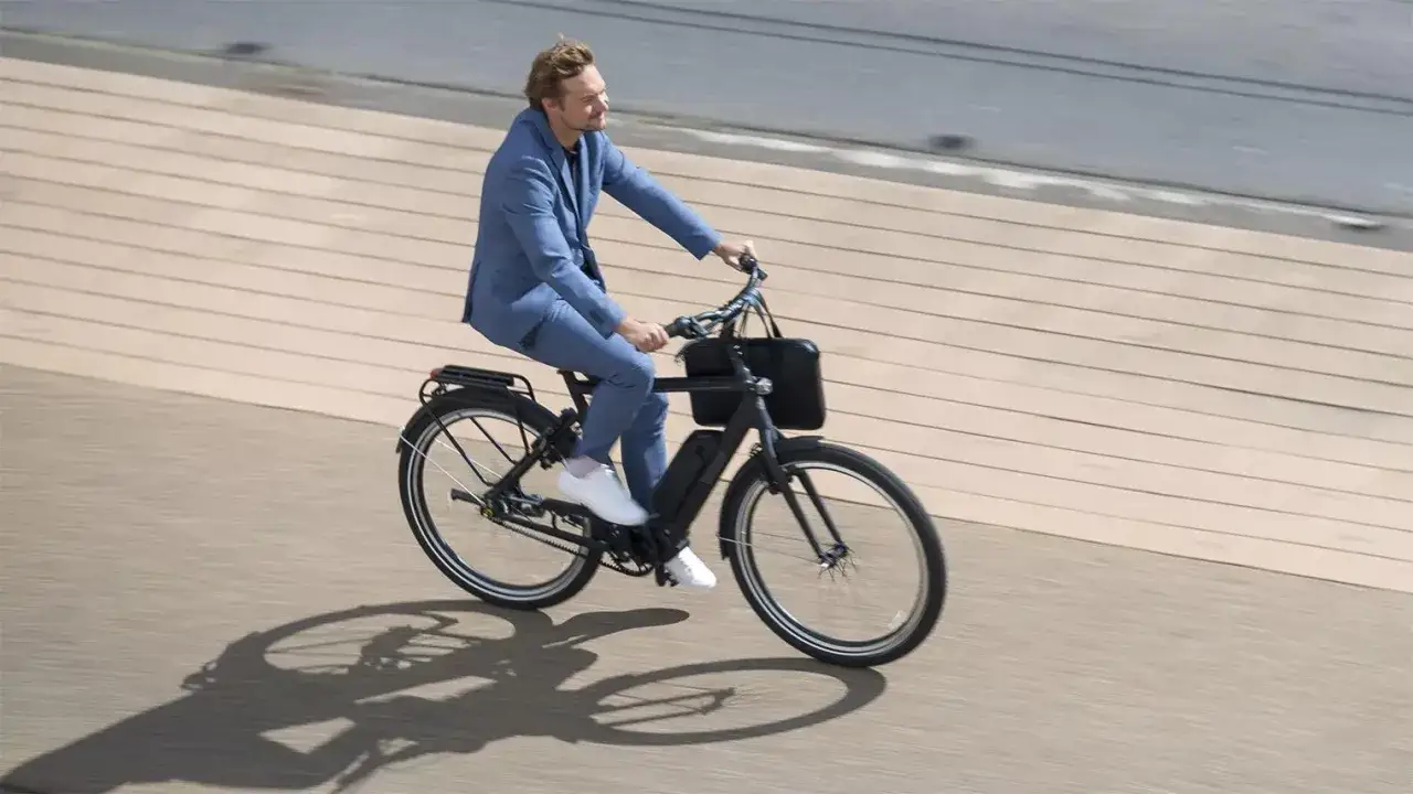 Man in blauw pak op een elektrische fiets, genietend van de rit. De actieradius van de elektrische fiets is ruim voldoende voor zijn dagelijkse woon-werkverkeer.