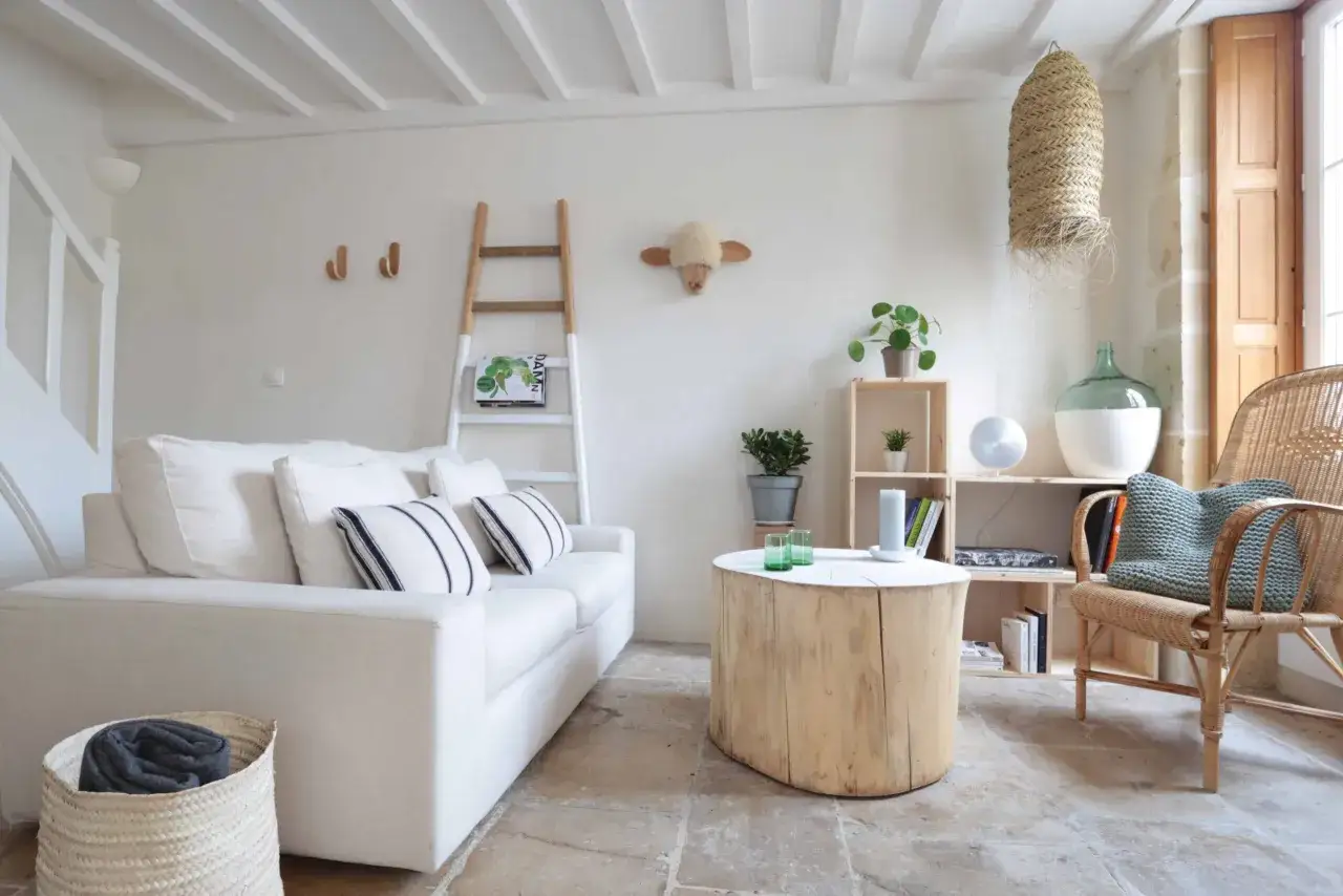 Salon lumineux d'une maison de pêcheur, avec canapé blanc, table en tronc d'arbre et fauteuil en rotin.