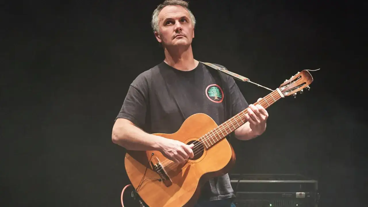 Un homme joue de la guitare sur sc&egrave;ne, son regard perdu dans le lointain, comme s'il contemplait le **mount eerie**.