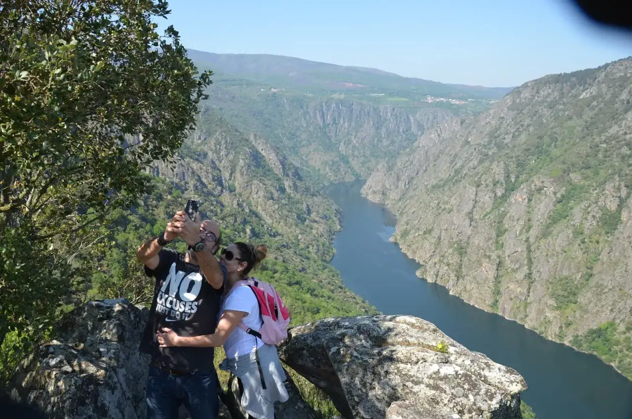 Pareja disfrutando de impresionantes rutas por Galicia, capturando un selfie con un cañón y río al fondo.