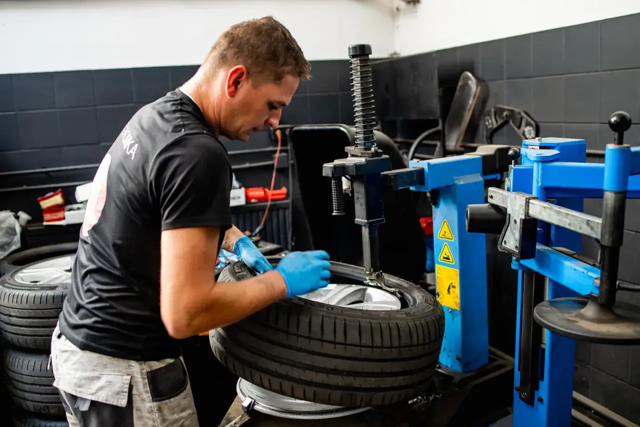 Mechanik w niebieskich rękawiczkach pracuje przy maszynie do wulkanizacji, wymieniając oponę.