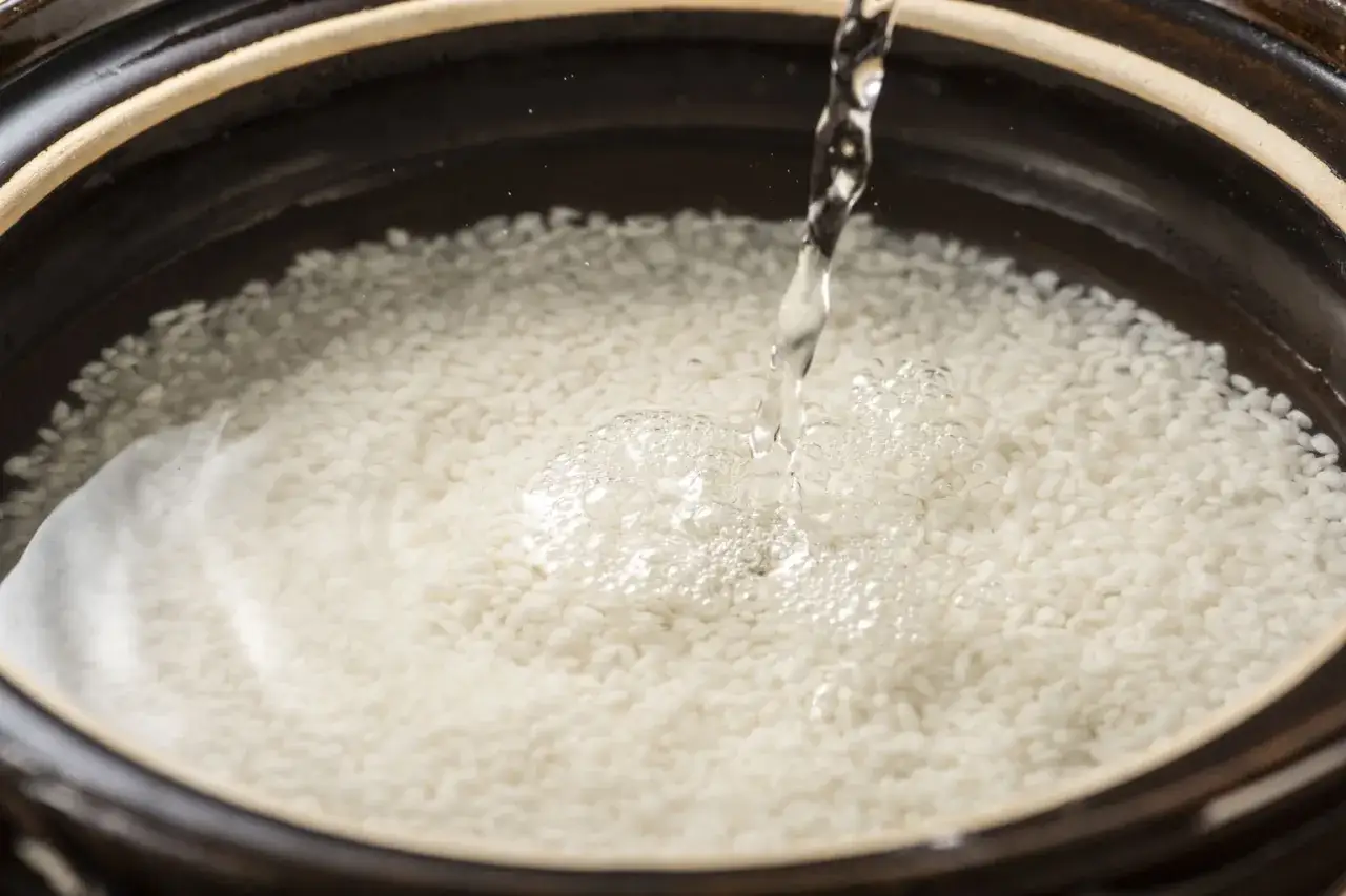 Acqua che scorre su chicchi di riso in una ciotola, preparando l'acqua di riso per capelli luminosi e forti.