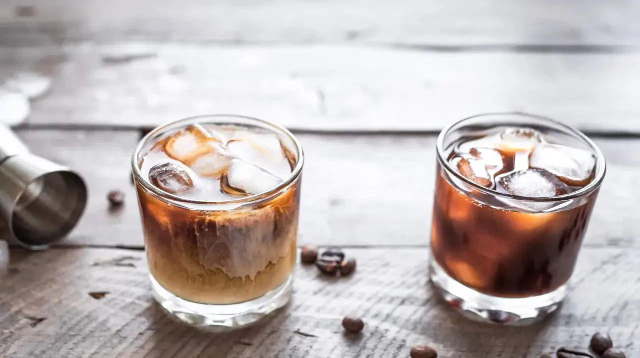 Dwa drinki na drewnianym stole: jeden to White Russian, drugi to Black Russian.