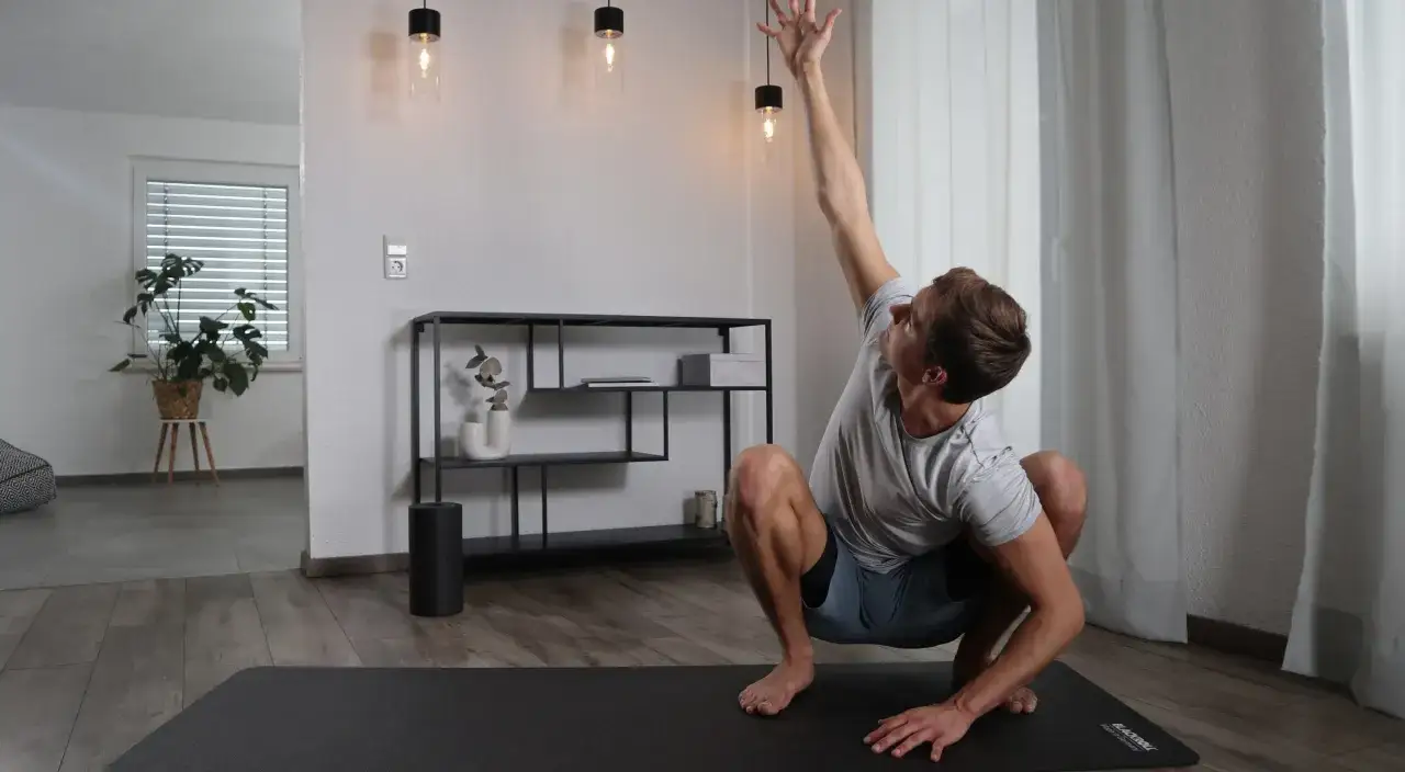 Mann macht Yoga-Übung auf Matte. Er streckt einen Arm nach oben. Perfekt, um nachts Sport zu machen und den Tag ausklingen zu lassen.