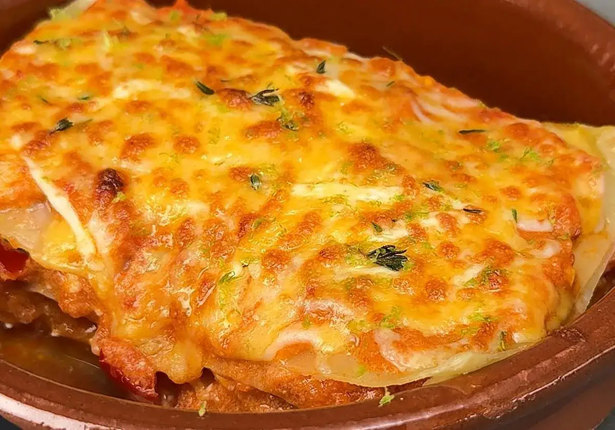 Deliciosa lasaña de atún gratinada, con queso dorado y hierbas frescas, servida en una cazuela de barro.