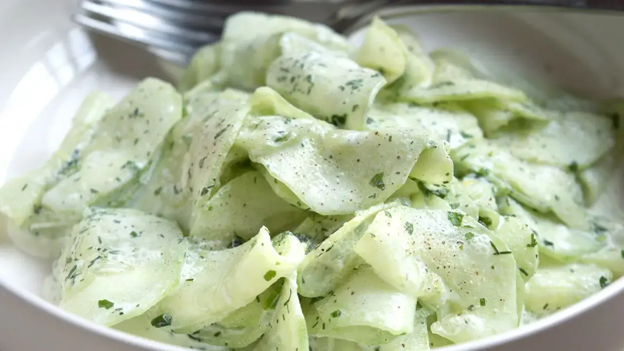 Cremiger gurkensalat ohne essig, mit frischer Petersilie und Pfeffer bestreut, serviert in einer weißen Schüssel.