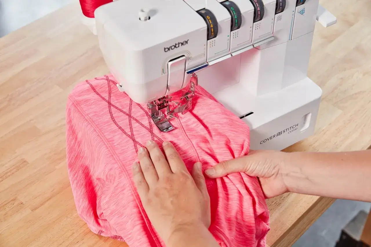 Hands guide pink fabric through a Brother coverstitch machine, creating decorative criss-cross stitching.
