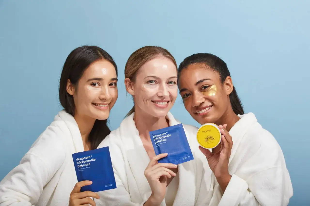 Tres mujeres sonríen con parches en los ojos, mostrando la preparación de la piel antes del maquillaje.