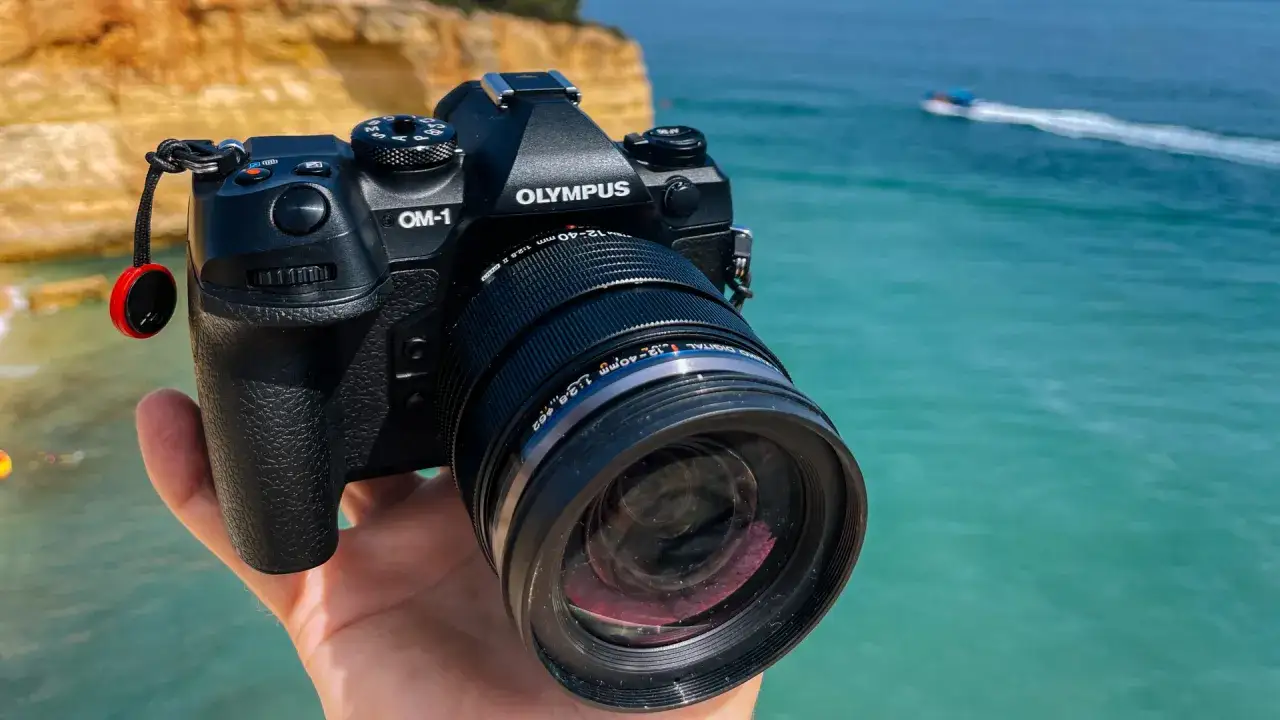 Olympus OM-1 z obiektywem 12-40mm na tle turkusowego morza i klifów. Idealny sprzęt na wakacyjne przygody.