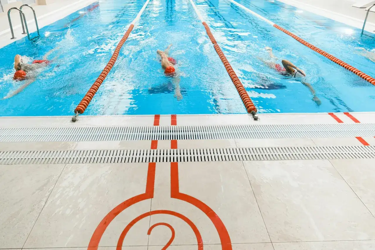 Schwimmer in roten Kappen trainieren im Schwimmbecken. Die Bahnen sind mit orangefarbenen Bojen markiert. Die durchschnittliche Zeit für 1 km schwimmen ist hier nicht ersichtlich.
