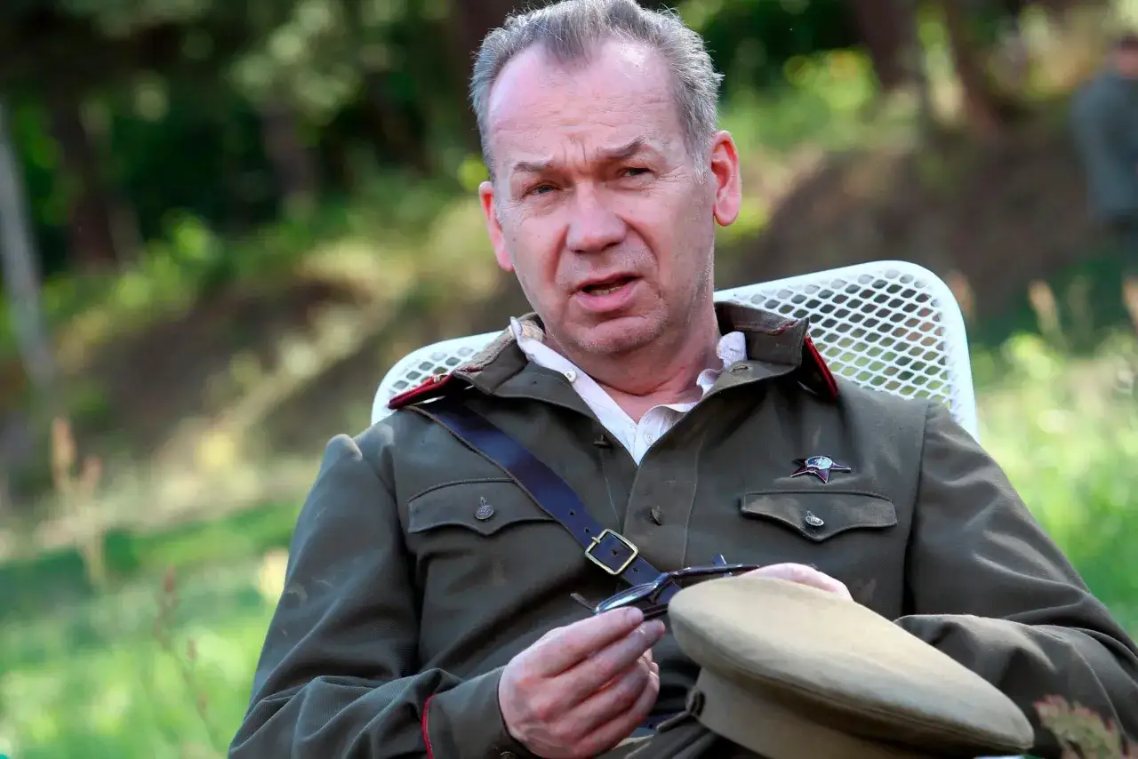 Mirosław Baka w wojskowym mundurze, przygotowuje się do roli w jednym z filmów. W rękach trzyma okulary i czapkę.