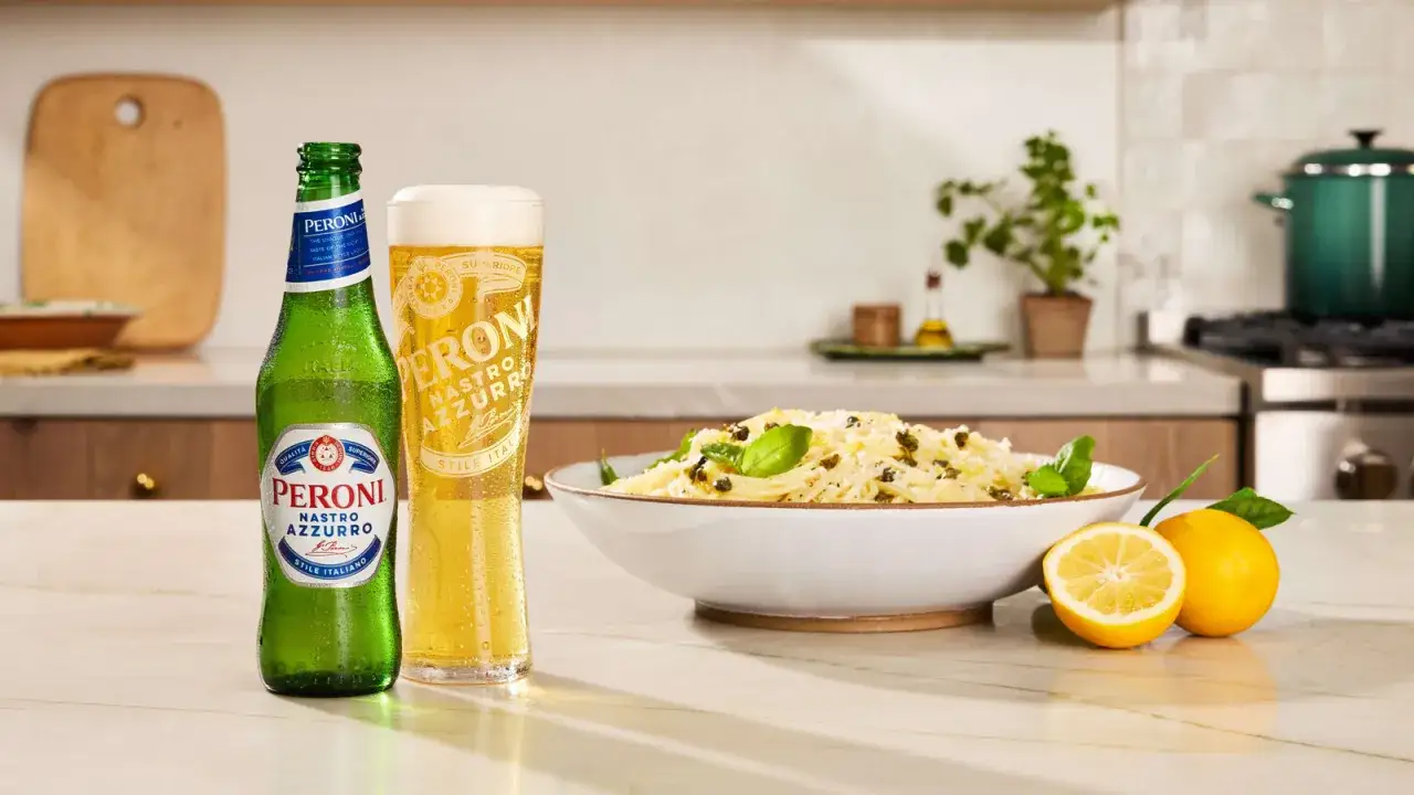 Peroni Nastro Azzurro, ein italienisches Bier, steht neben einem Teller Pasta und Zitronen auf einem Küchentisch.