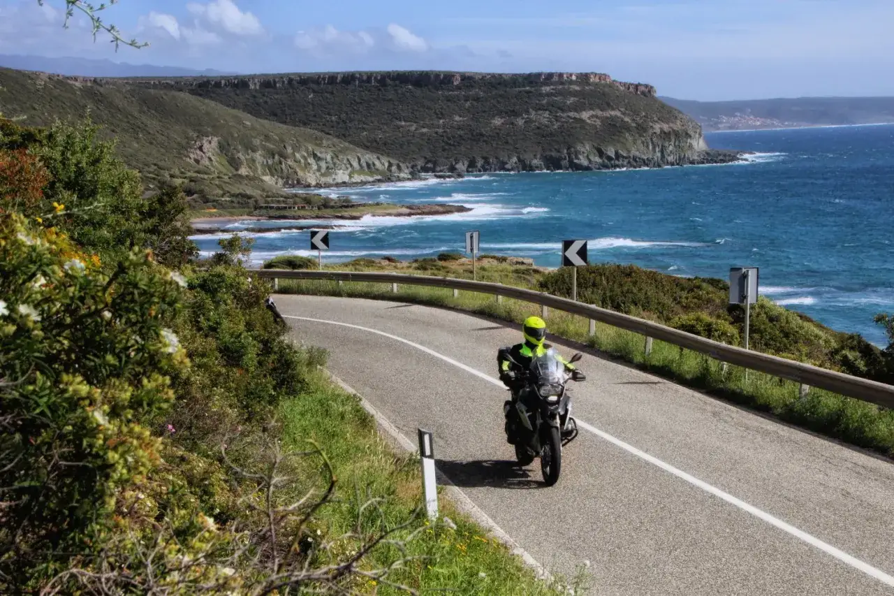 Motocyklista przemierza malowniczą trasę na Sardynii, podziwiając błękitne morze i skaliste wybrzeże.