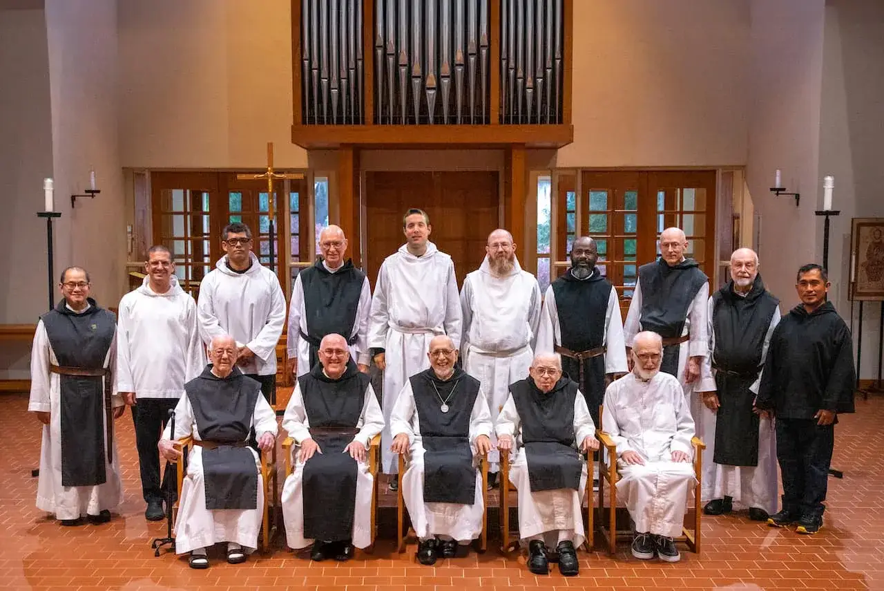 A group of monks, including the monastery leader, pose for a formal portrait in front of an organ.