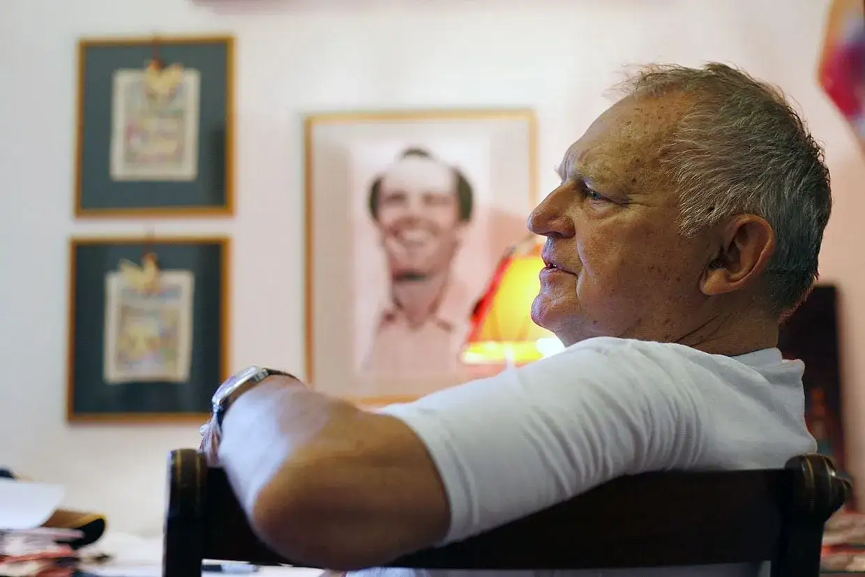 Jerzy Gruza, twórca kultowych filmów, seriali i programów, siedzi w fotelu, w tle jego portret.