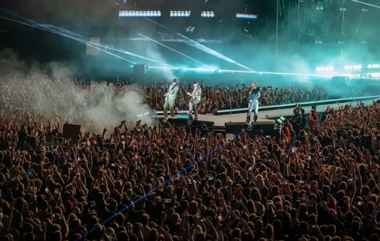 Koncert Linkin Park Polska. Tłum fanów z rękami w górze, światła sceniczne i dym tworzą niesamowitą atmosferę.