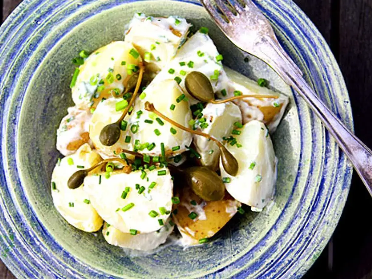 En sk&aring;l med kr&auml;mig, hemmagjord potatissallad med kapris och gr&auml;sl&ouml;k. En gaffel ligger bredvid.
