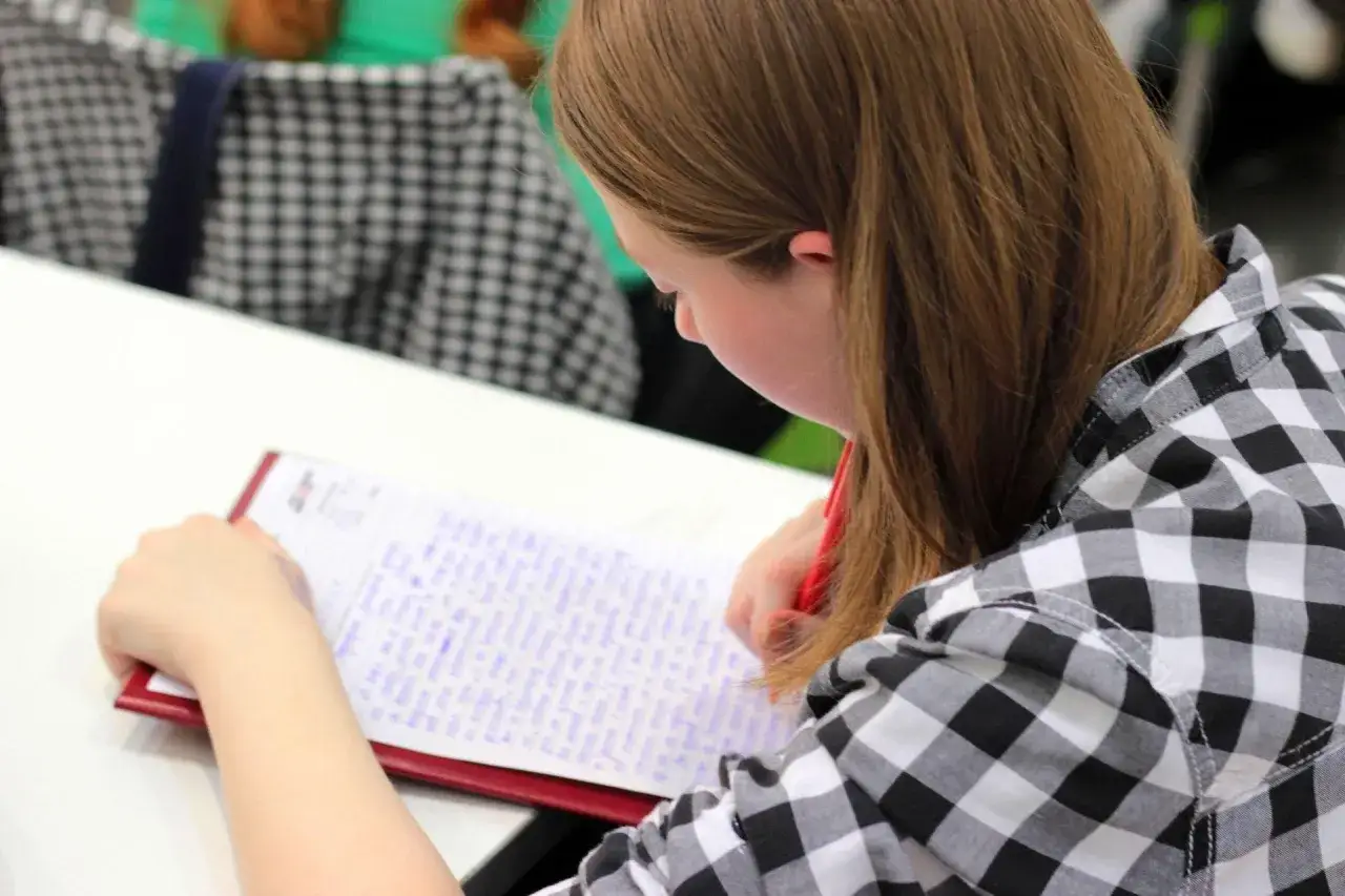 Chica concentrada en su dictado 1 eso, escribiendo en un cuaderno con bol&iacute;grafo rojo.