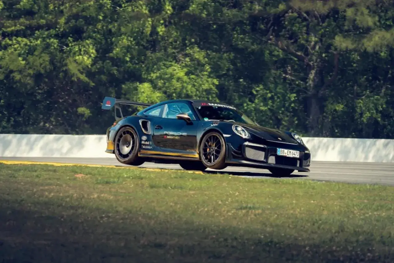 Czarny Porsche 911 GT2 RS na torze wyścigowym, z zielonymi drzewami w tle.