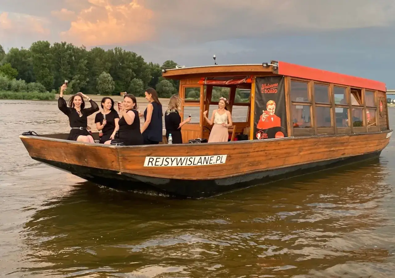 Grupa kobiet świętuje na łodzi podczas rejsu po Wiśle w Płocku. Wesoła atmosfera i zachód słońca tworzą niezapomniane wspomnienia.