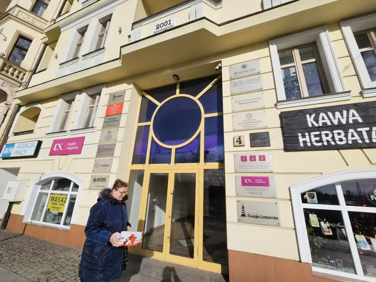 Kobieta z pudełkiem Kinder Bueno pod biurem poselskim PiS w Warszawie. Na budynku widnieje rok 2001.