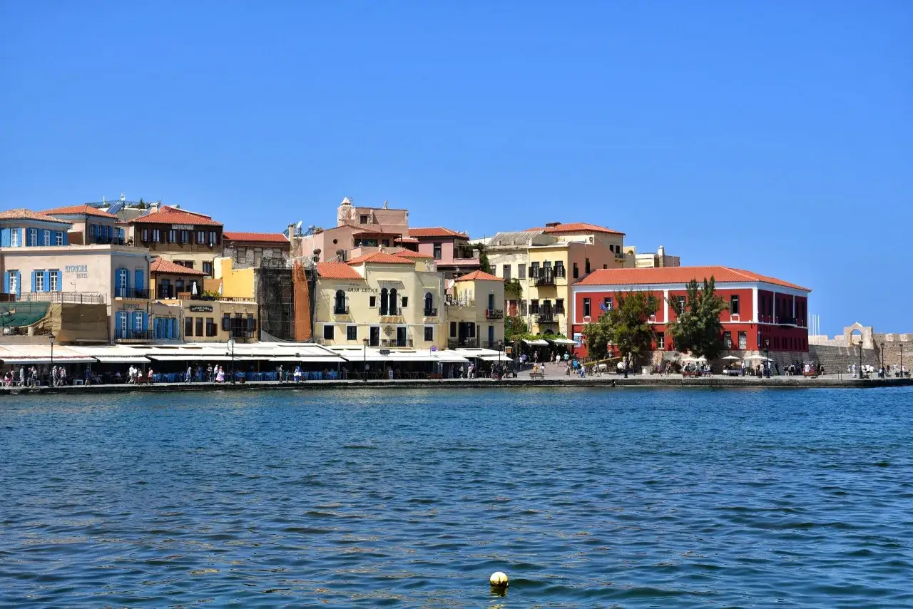 Kolorowe budynki w Chania stare miasto nad wodą, z ludźmi spacerującymi promenadą i siedzącymi w kawiarniach.