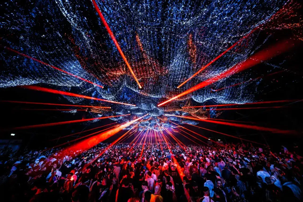 Folla in delirio sotto un soffitto di luci rosse e blu, immersa nel ritmo delle canzoni techno.