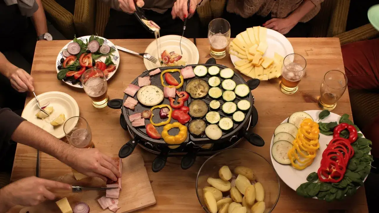 Una cena de raclette con amigos. El queso se derrite sobre la parrilla, junto a verduras y carnes.