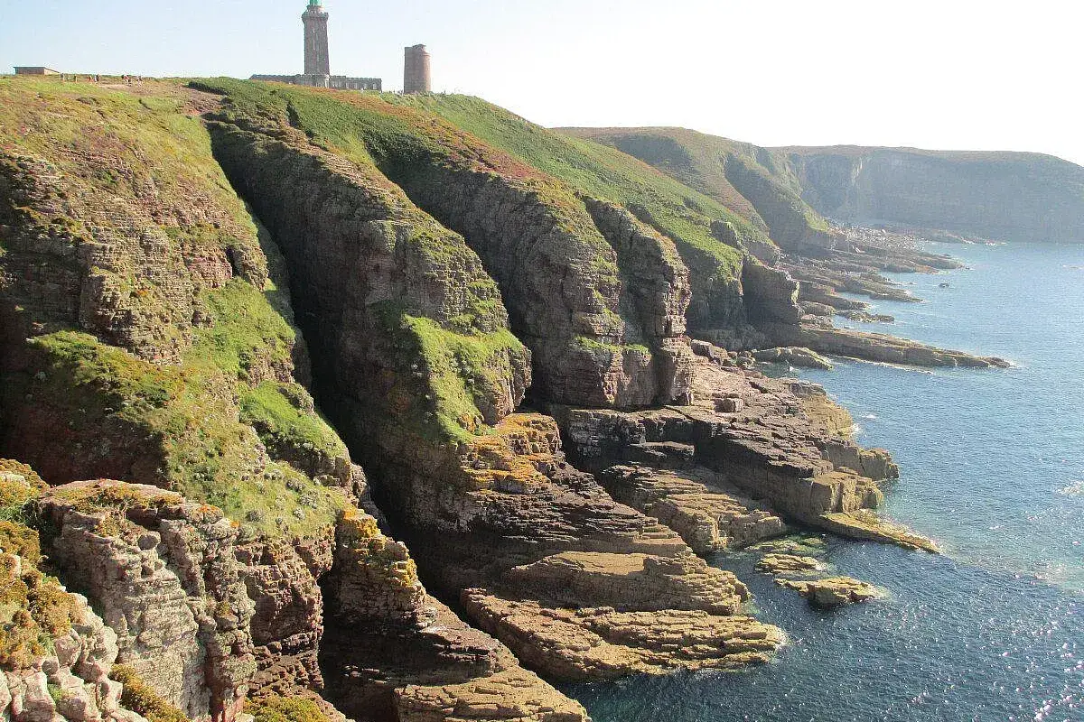 Scogliere verdi e rocciose con un faro in cima. Ideale per consigli di **Bretagna in moto**.