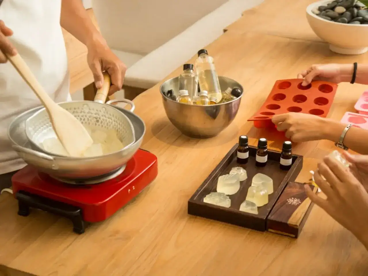 Mani che preparano sapone fatto in casa, sciogliendo ingredienti in un pentolino e versandoli in stampini. Olio essenziale e stampi pronti.