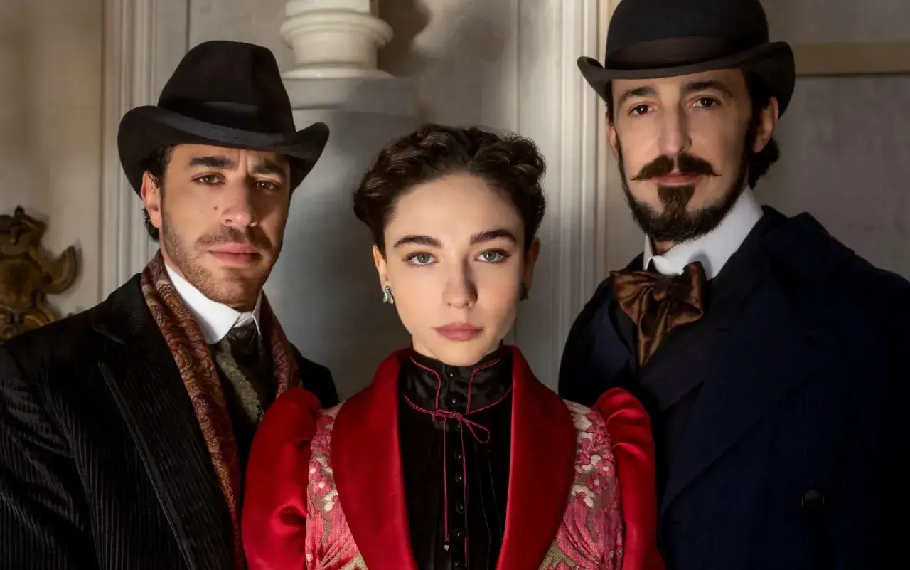 Lidia poet serie: tre figure eleganti in abiti d'epoca, un uomo a sinistra, una donna al centro e un uomo a destra.
