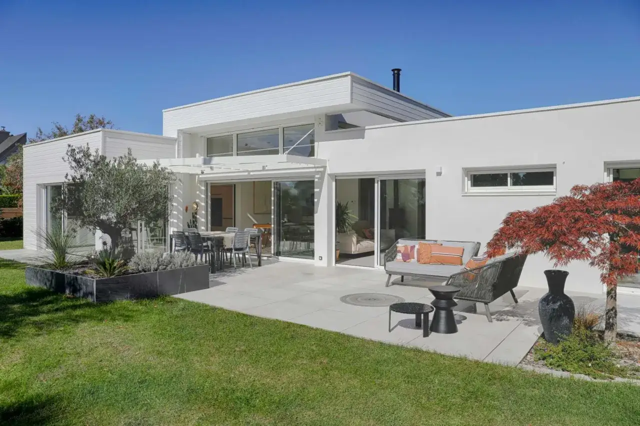 Maison moderne avec extension. L'architecte a conçu un espace de vie extérieur invitant, avec terrasse, mobilier confortable et jardin. L'extension maison architecte obligatoire est une réussite.