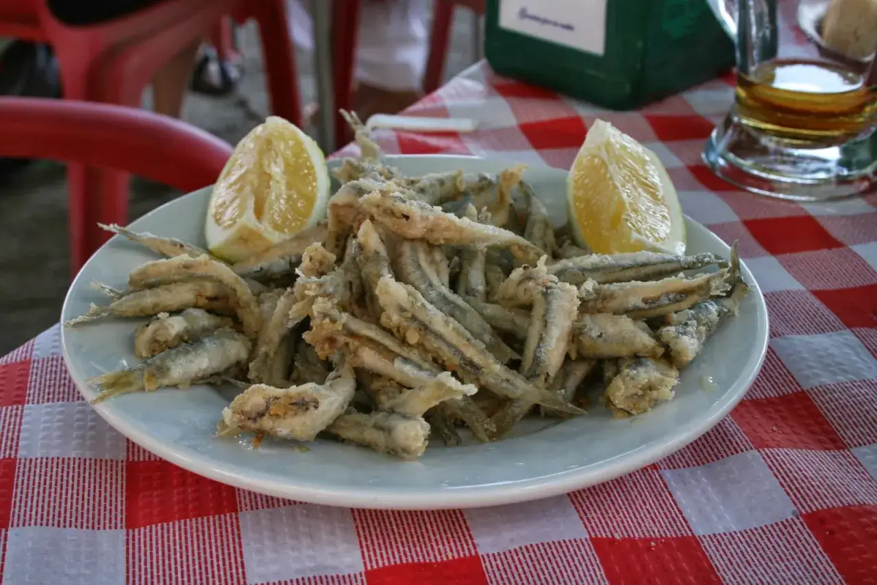 Un plato de fritura de pescado crujiente, adornado con gajos de lim&oacute;n, listo para disfrutar en una mesa a cuadros.