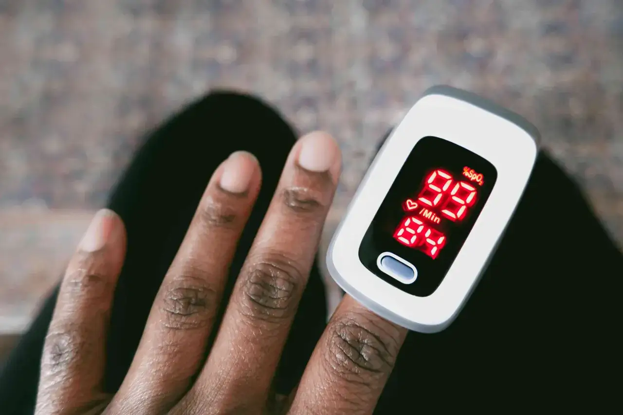Fingerspitze mit Pulsoximeter, das 99% Sauerstoffs&auml;ttigung und 84 Schl&auml;ge pro Minute anzeigt. Kein Hinweis auf zuviel Sauerstoff im Blut.