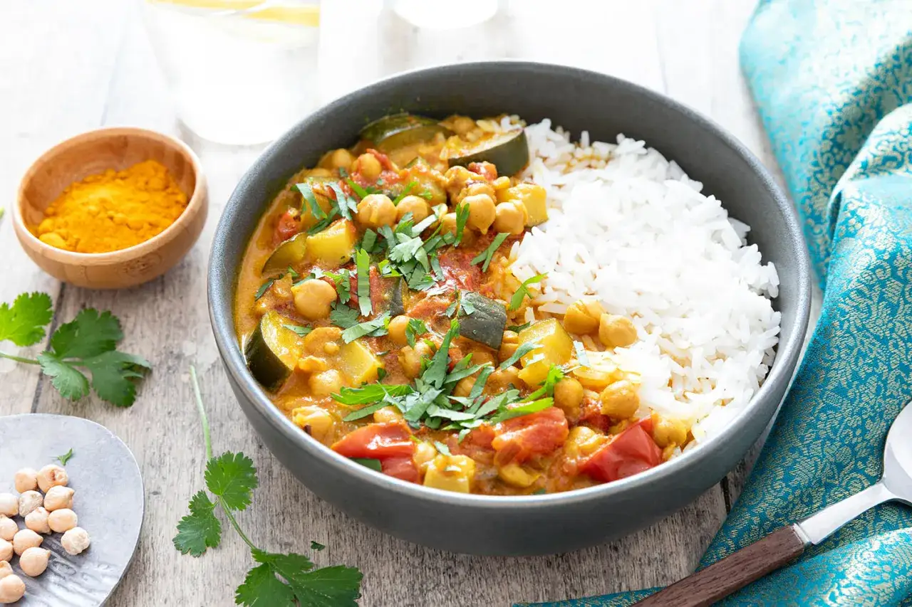 Un savoureux curry de l&eacute;gumes avec pois chiches, courgettes et tomates, servi avec du riz blanc et garni de coriandre fra&icirc;che.